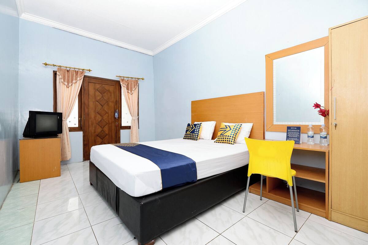 A bedroom with a bed, a TV, a desk, and a mirror.