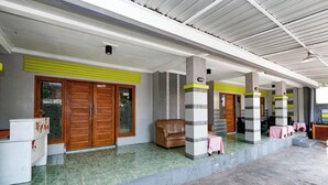 A covered outdoor area with a reception desk, wooden doors, a brown leather sofa, and tables with pink checkered tablecloths.