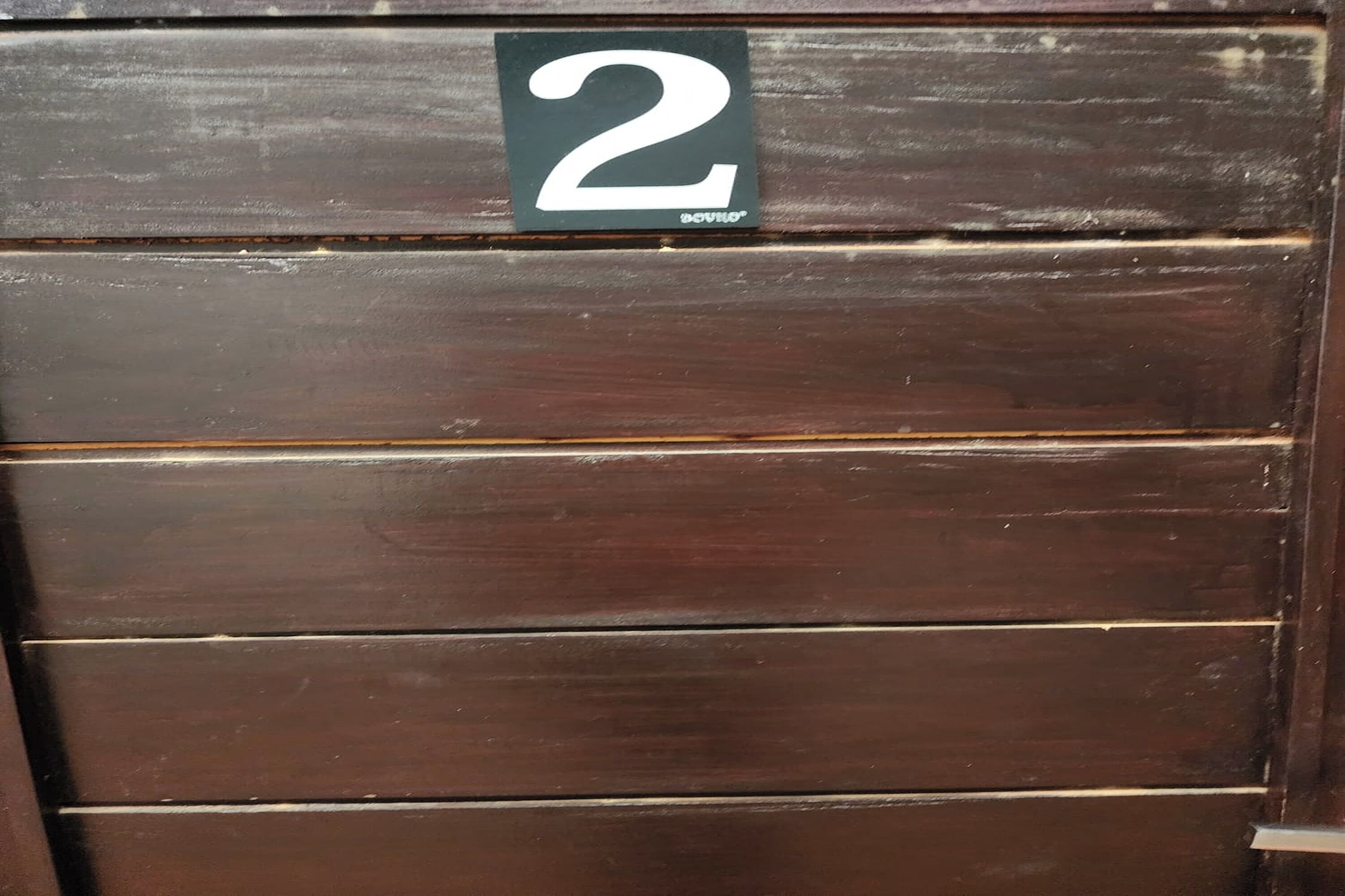 Une porte en bois sombre, composée de planches disposées horizontalement, et sur laquelle est apposé un panneau indiquant le numéro 2.