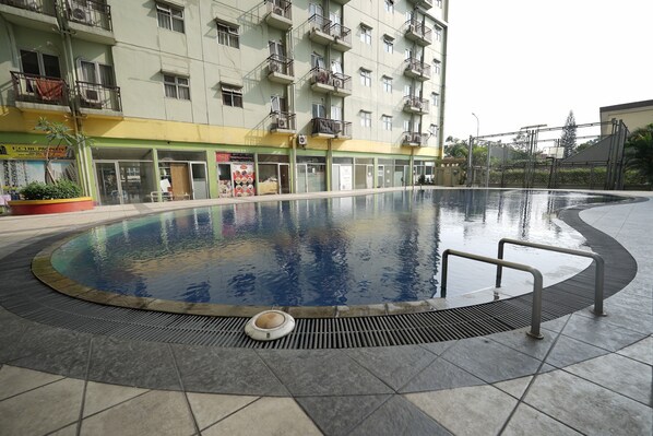 Una piscina con borde de azulejos, rodeada por un edificio con varios balcones y una fachada comercial.