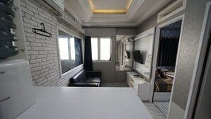 A compact, modern room with a white countertop, a black sofa, a small window, and a door leading to another room. - Perfect Stay Apartement The Suites Metro Bandung By Sultan Property (Bandung)