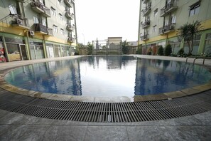 Una piscina con borde de baldosas, rodeada de edificios de varios pisos con balcones y unidades de aire acondicionado.