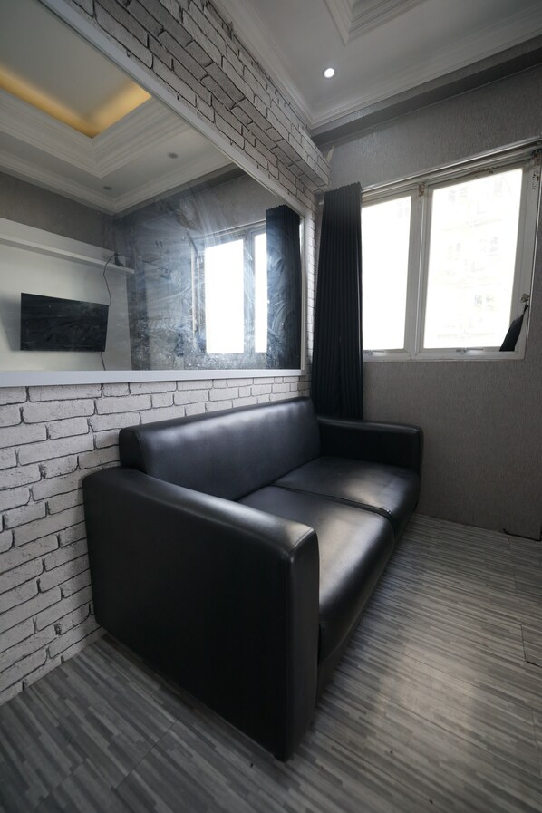 A modern room with a black leather sofa, a white brick accent wall, and a large window with curtains. - Perfect Stay Apartement The Suites Metro Bandung By Sultan Property (Bandung)