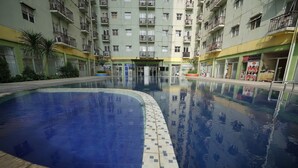 A swimming pool with tiled edges, surrounded by a multi-story building with balconies and shops on the ground floor. - Perfect Stay Apartement The Suites Metro Bandung By Sultan Property (Bandung)