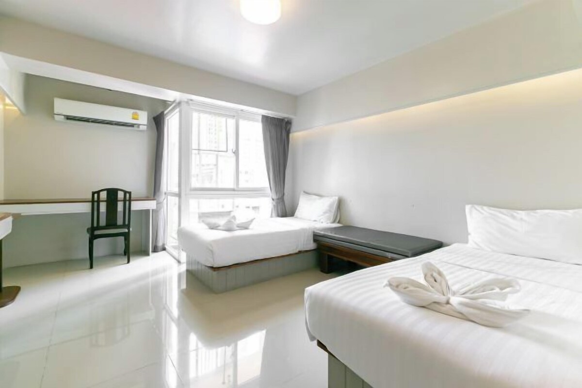 A hotel room with a bed, a desk, a chair, and a window with curtains.