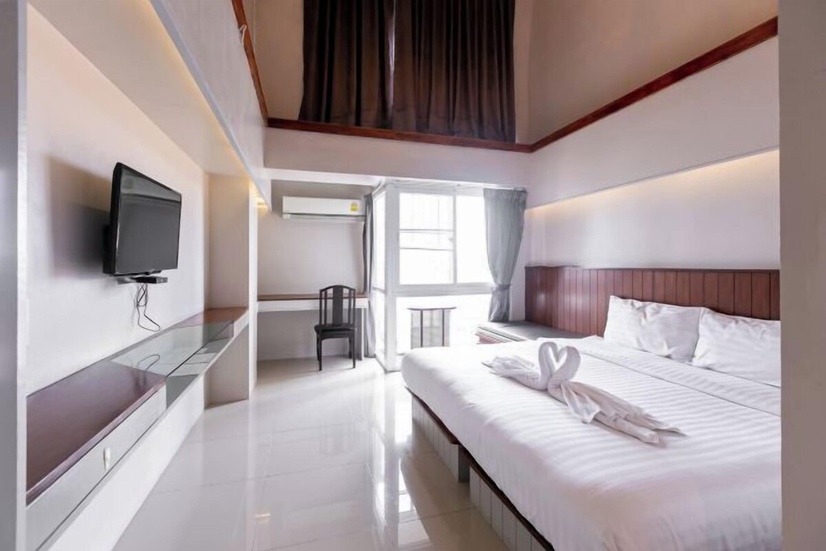A modern hotel room with a large bed, a flat-screen TV mounted on the wall, a desk, and a chair.