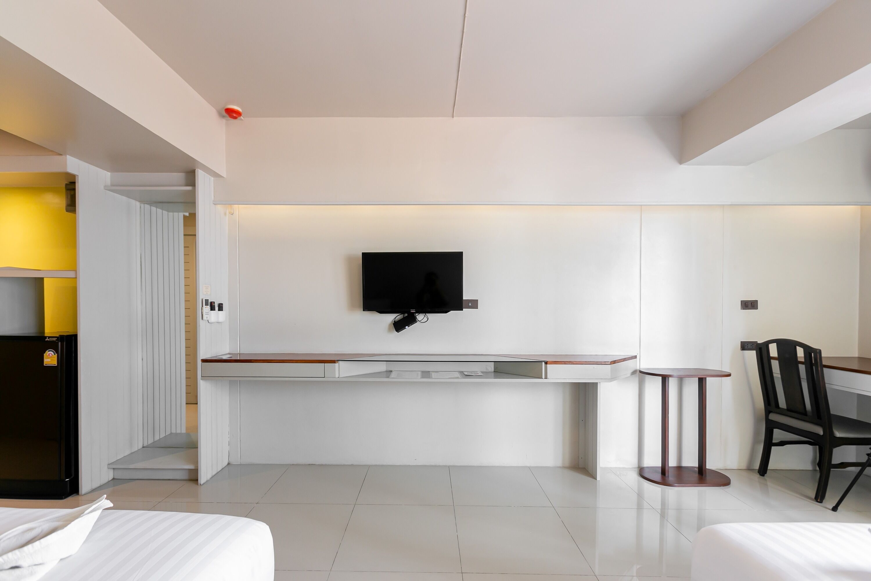 A hotel room with a bed, a desk, a chair, a TV mounted on the wall, and a small table.