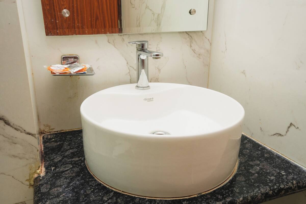 A bathroom with a white sink, a mirror, and a soap dispenser on a shelf.