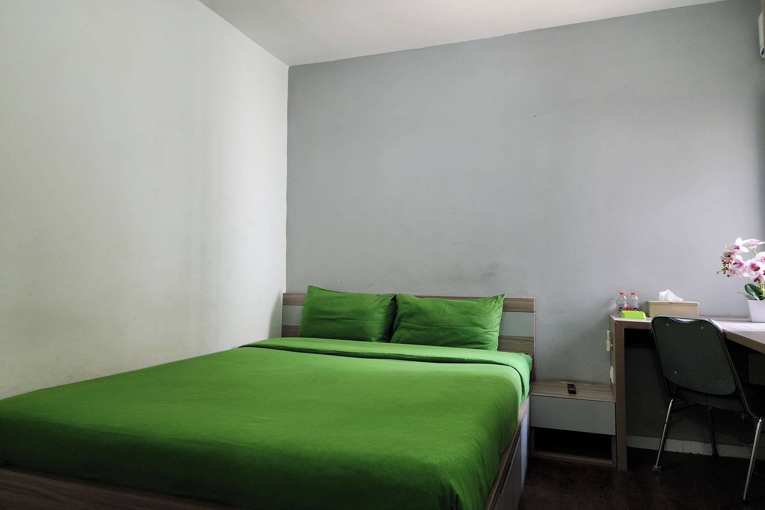 Un dormitorio con una cama, un escritorio, una silla y una pequeña mesa con un florero.