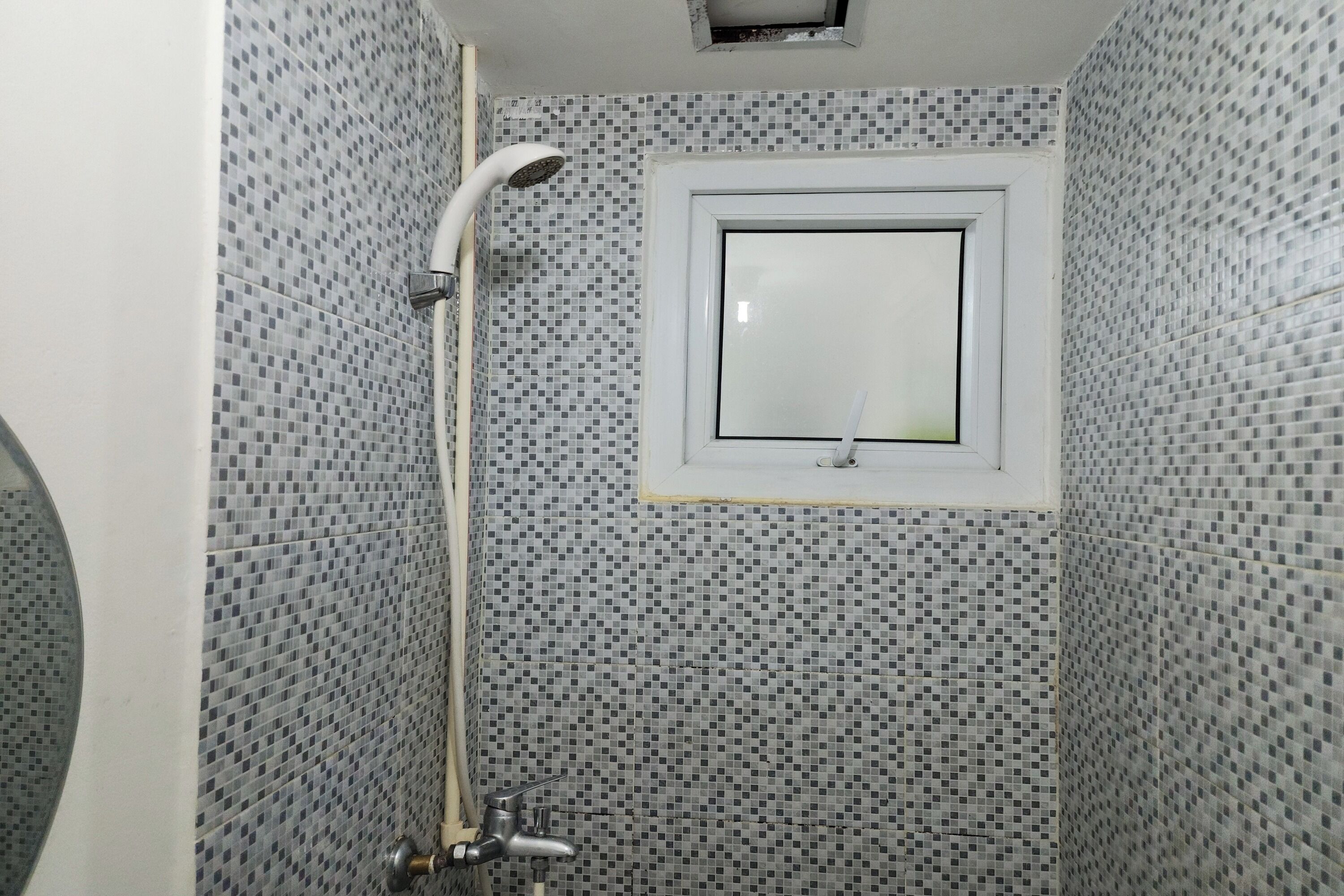 A small bathroom with mosaic tile walls, a showerhead, and a window with a mirror.