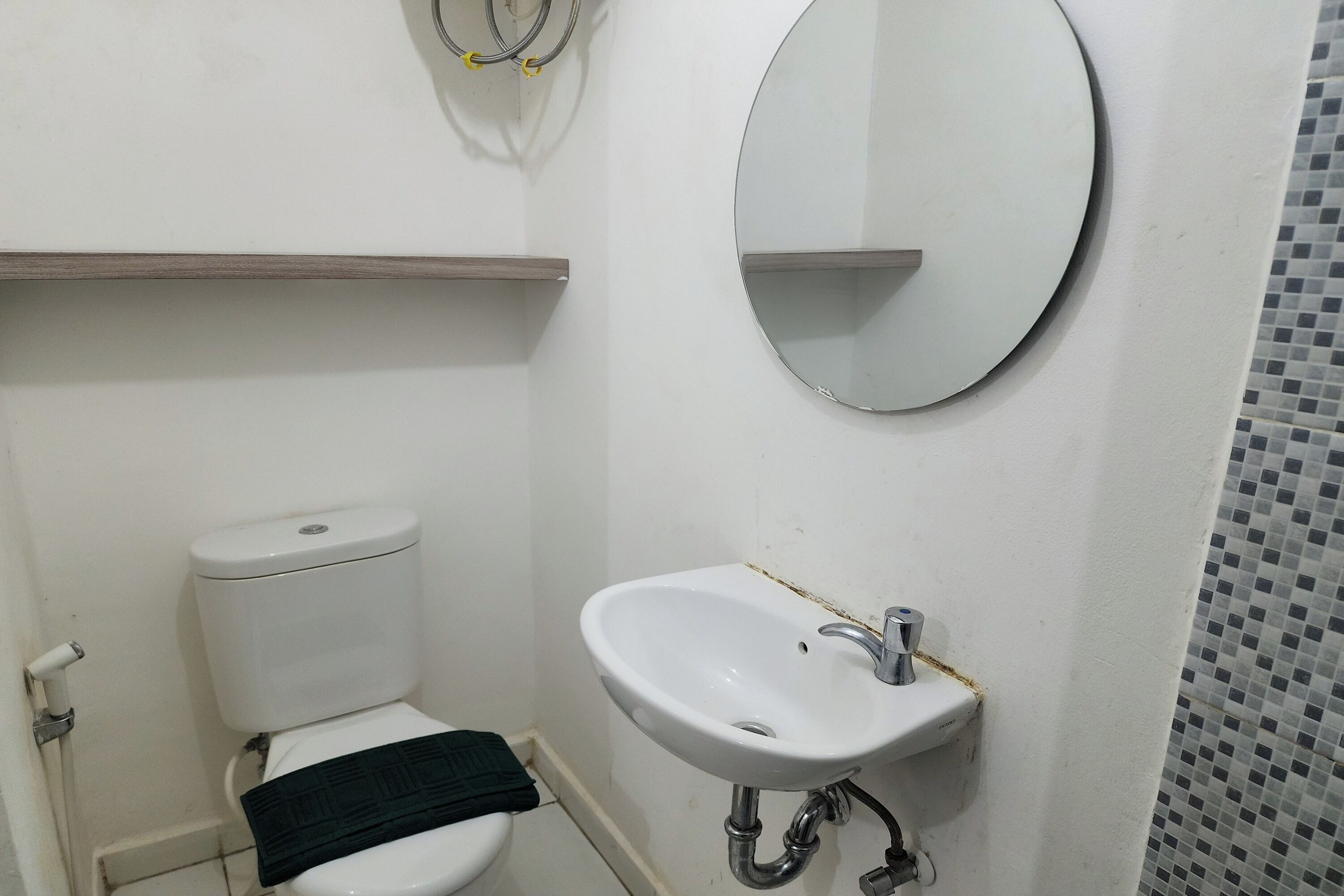 A small bathroom with a white toilet, a white sink with a mirror above it, and a tiled shower area.