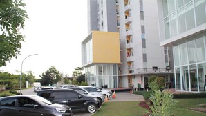A modern building with a yellow section, surrounded by a parking area with several cars.
