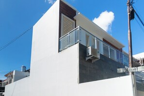 A modern building with a white facade, a balcony with glass railings, and a visible air conditioning unit. - Villa Berlian (Kuta)