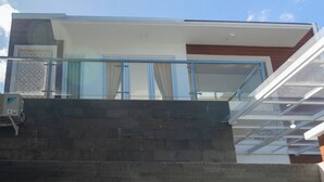 Un edificio moderno con un balcone in vetro, un muro in pietra e un pannello in legno al piano superiore.