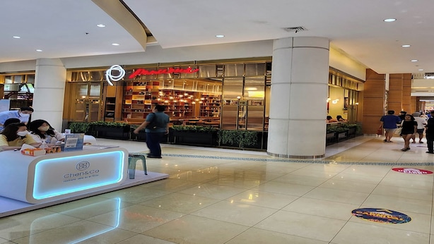 A modern hotel lobby with a reception desk, a restaurant with a red sign, and a clean, tiled floor. - Heritage Home (Gading Serpong)