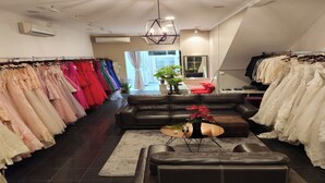 A bridal boutique with rows of dresses on racks, a black leather sofa, and a hanging light fixture. - Heritage Home (Gading Serpong)