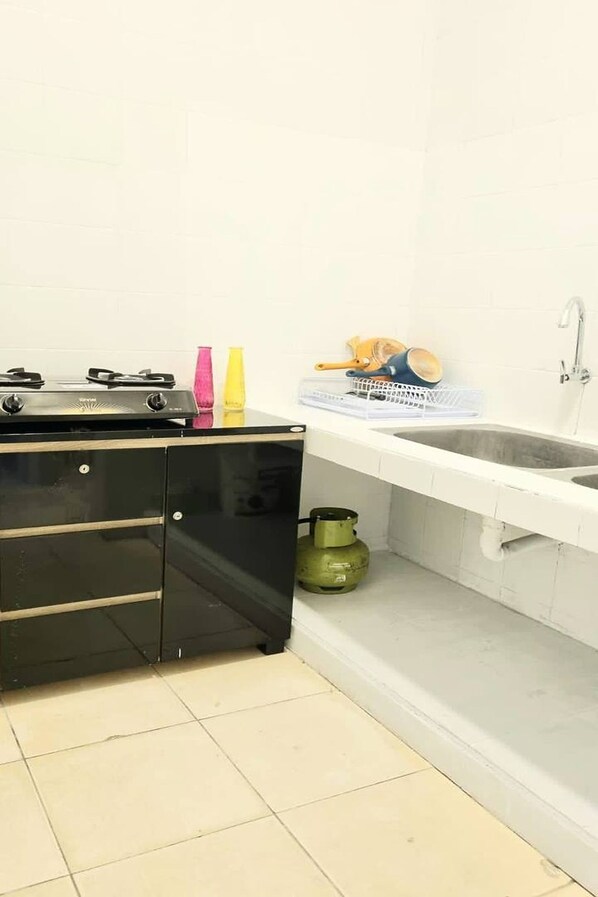A kitchen with a black stove, a sink, and a gas cylinder. - Heritage Home (Gading Serpong)
