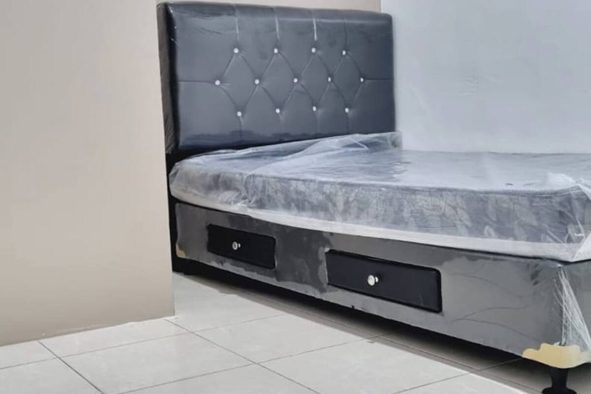 A corner bedroom with a bed, a small drawer, and a tiled floor.