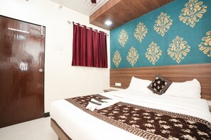 A hotel room with a wooden door, a bed with white bedding and a patterned throw, a red curtain, and a wall with a decorative blue and gold design. - Hotel Mumbai Residency (Mumbai)