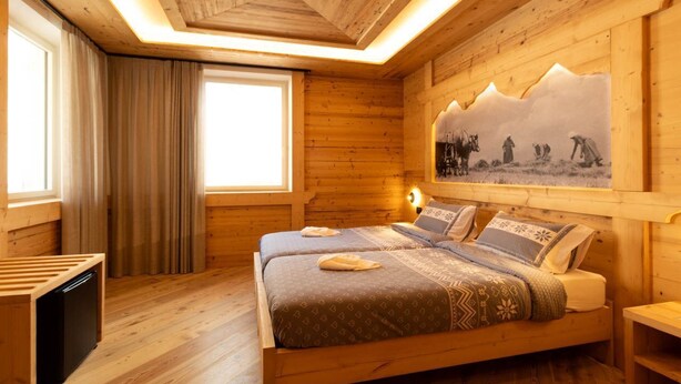 Una habitación de madera con una cama, una ventana con cortinas y un cuadro en la pared.