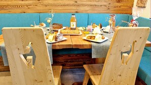 Un rincón comedor acogedor de madera con un banco acolchado azul, sillas de madera y una mesa servida con diversos pasteles y una botella de hidromiel.