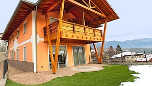 Una casa moderna con balcón de madera, fachada de piedra y vistas a montañas.
