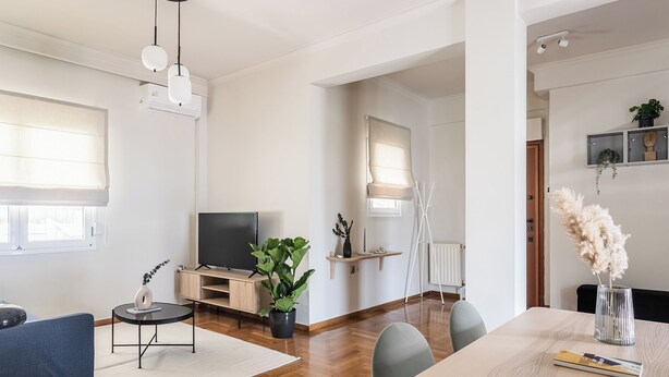 A modern living room with a flat-screen TV, a blue sofa, a dining table with chairs, and a potted plant. - Harmonious 2BR Apartment in Exarchia (Athens)
