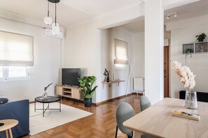 Un salon moderne avec un téléviseur à écran plat, un canapé bleu, une table à manger avec des chaises et une plante en pot.