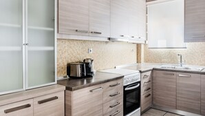 A modern kitchen with light wood cabinets, a tiled backsplash, a stove, and a coffee maker. - Harmonious 2BR Apartment in Exarchia (Athens)