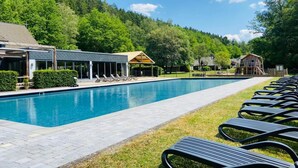 Una piscina con sillas de descanso, una zona cubierta y un promontorio boscoso al fondo.
