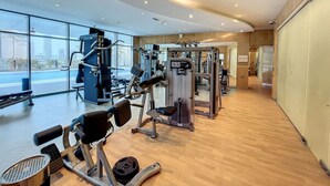 A modern gym with various exercise machines, large windows, and a wooden floor. - Gorgeous 1 Bed l City Views l near Media City Park (Dubai Marina)