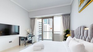 A hotel room with a large bed, a desk, a chair, a TV, and a balcony with curtains. - Gorgeous 1 Bed l City Views l near Media City Park (Dubai Marina)