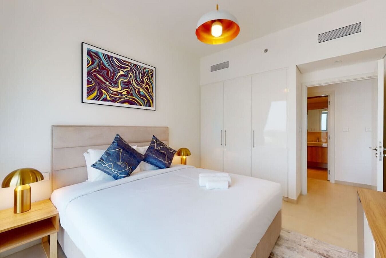A modern hotel room with a large bed, a wardrobe, and a painting on the wall.