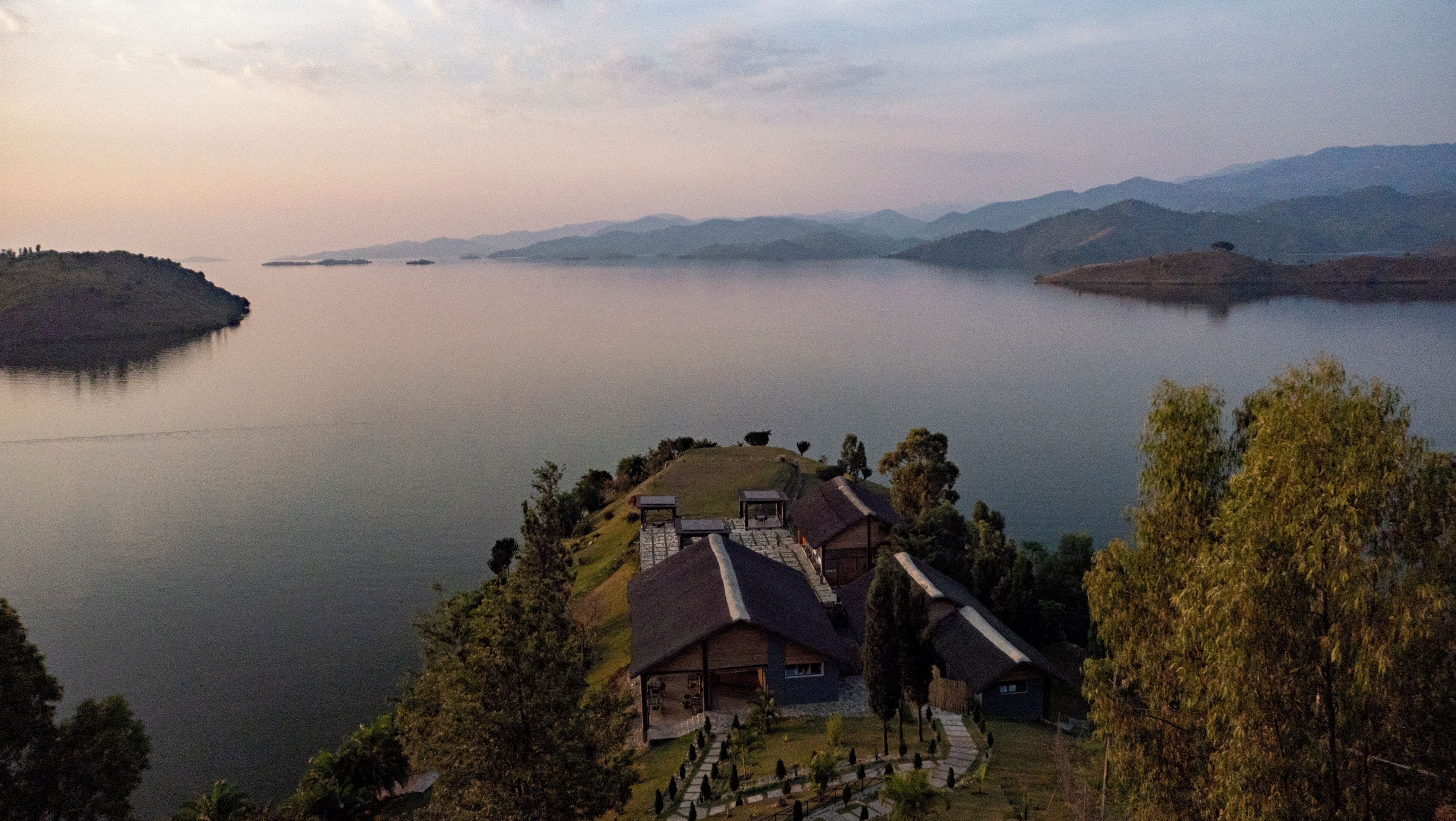 A lakeside property with a house featuring a stone roof, a patio, and a view of the lake and mountains.