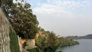 Una escalera de piedra conduce a una terraza con vistas a un lago, rodeada de vegetación exuberante y un cielo despejado.