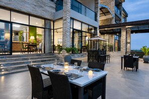 Un espacio moderno para comer al aire libre con fachada de piedra, ventanas grandes y vista al interior.