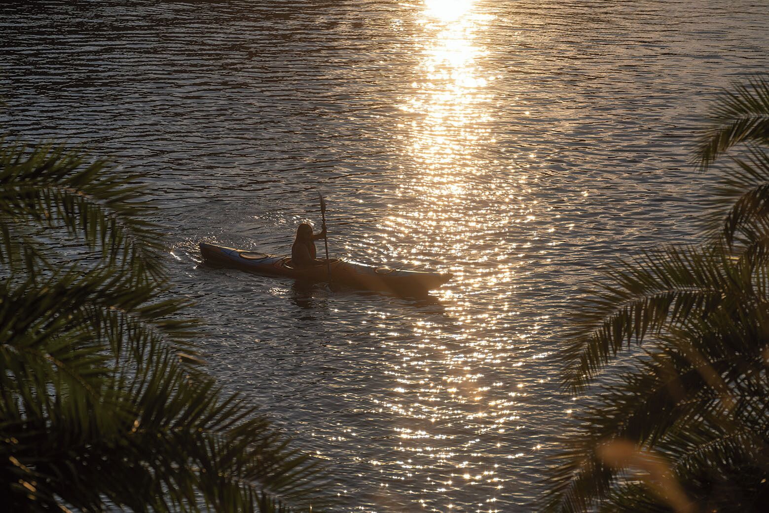 A person kayaking on calm water with sunlight reflecting off the surface.
