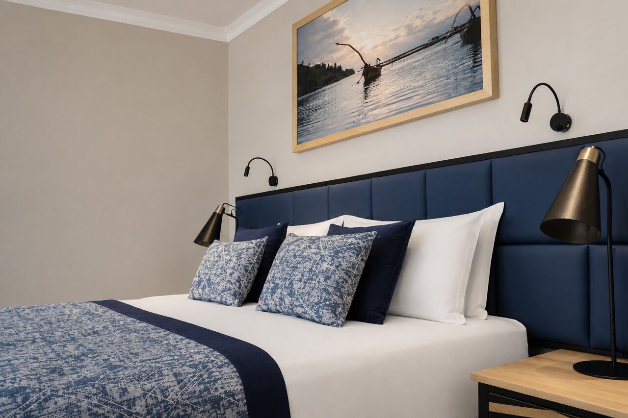Ein Hotelzimmer mit Bett, Nachttisch, Lampe, einem Gemälde und Kopfhörern.