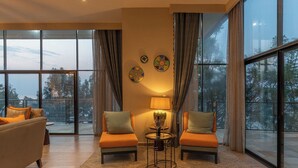 A modern living room with large windows, a sofa, two armchairs, a small table with a lamp, and decorative wall art. - LUX* Lake Kivu (Bwishyura)