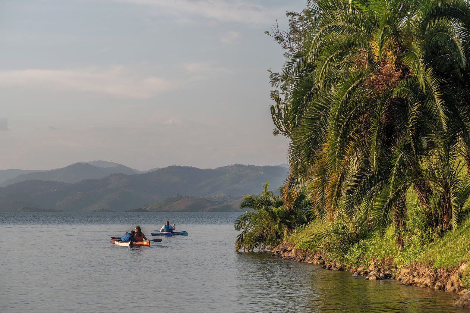Un lac paisible où voguent des bateaux, entouré d’une végétation luxuriante et dominé par des collines lointaines.