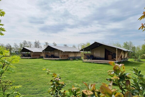 Une rangée de chalets à un seul étage, dotés de vérandas ouvertes, s’étend sur une pelouse bien entretenue, le tout étant entouré d ’arbres.
