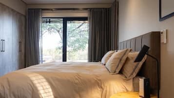Une chambre à coucher avec un grand lit, une table de chevet, une lampe et une vue sur l’extérieur par une fenêtre.