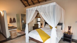 A four-poster bed with white bedding and a yellow throw, a bedside table with a vase, and a wicker basket on the floor. - Luxury villa with a swimming pool in Hoedspruit (Hoedspruit)