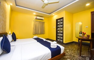 A hotel room with two beds, a ceiling fan, an air conditioning unit, a mirror, and a small table with flowers.