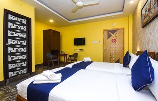 A hotel room with two beds, a desk, a chair, a television, and a ceiling fan.