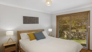 A bedroom with a bed, two bedside tables, a wall-mounted artwork, and a window with blinds. - Bella Vista Valley Views (BLACKHEATH)