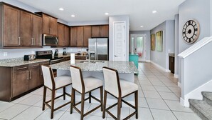 A modern kitchen with dark wood cabinets, a granite countertop, and a central island with bar stools. - Elegant Home near Disney: Private Pool & Waterpark & Resort - 7610WI (Kissimmee)