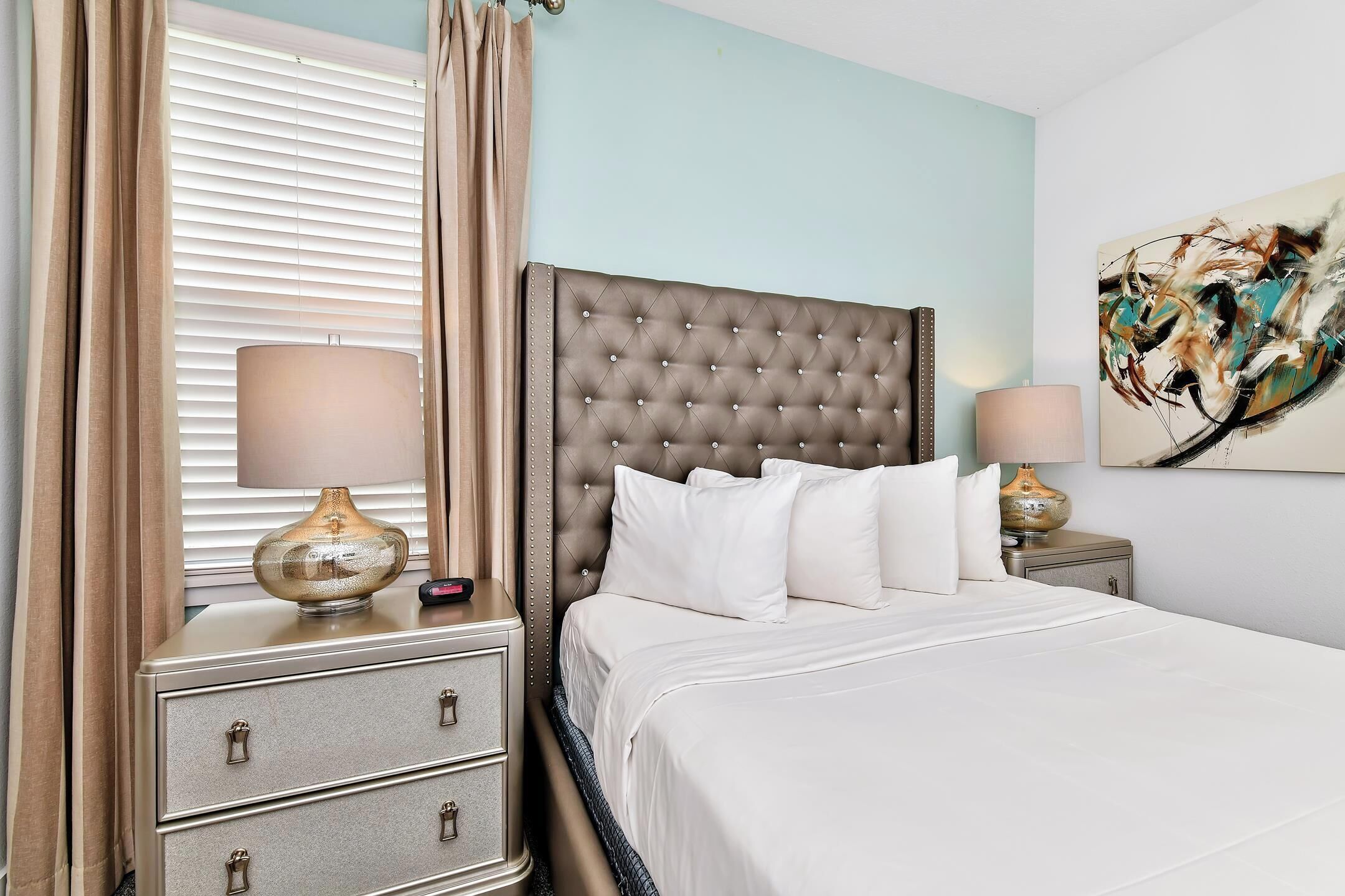 A neatly made bed with a tufted headboard, a bedside lamp, and a nightstand with drawers.