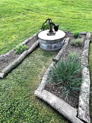 A garden with a concrete planter, wooden borders, and a metal watering fixture.
