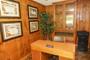 A wooden-paneled room with a desk, framed certificates on the wall, and a plant.